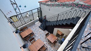 Une terrasse sur le toit, dotée de tables et de chaises en bois, d’un escalier avec une rampe en métal et d’un mur décoratif orné de motifs floraux.
