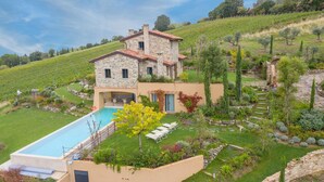 Una casa de piedra con piscina, rodeada de un jardín cuidado y un viñedo.