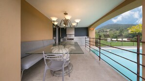 Un balcón con una mesa de vidrio, sillas, un sofá, una lámpara colgante y vista a la piscina.