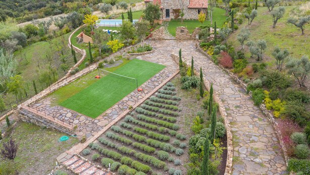 Una casa de piedra con jardín, cancha de tenis y viñedos al fondo.