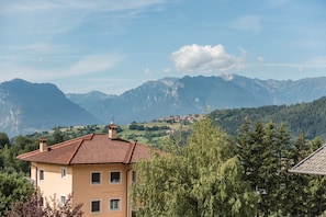 Un bâtiment coiffé d’un toit recouvert de tuiles rouges, entouré d’arbres et avec des montagnes en arrière-plan.
