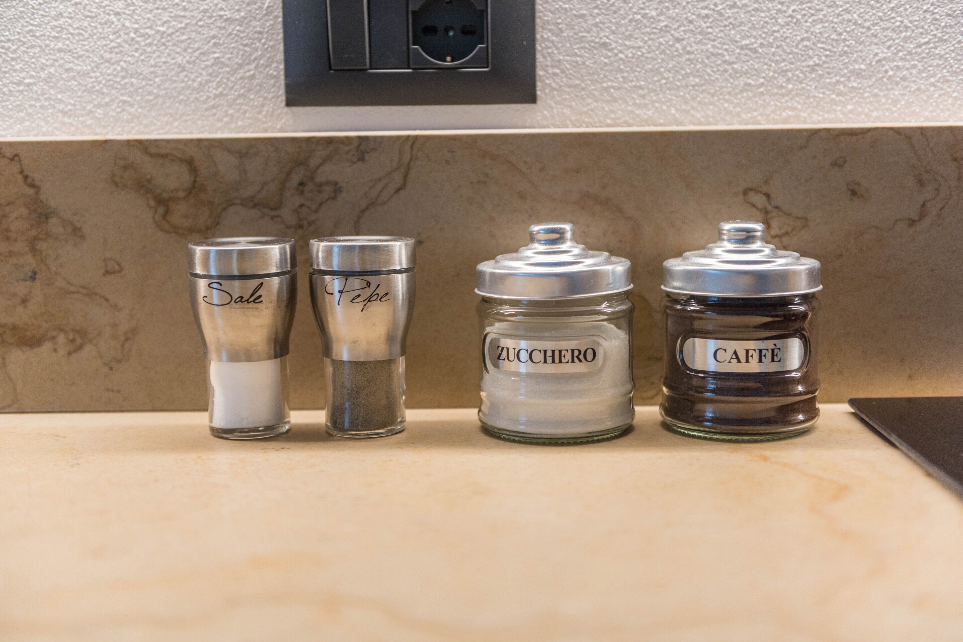 Four glass containers on a kitchen counter with labels 'Sale,' 'Pepe,' 'Zucchero,' and 'Caffè.'