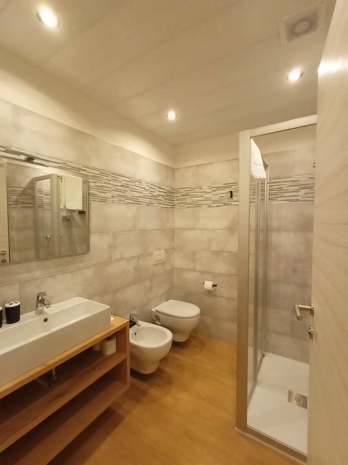 Un baño moderno con un espejo grande, un lavamanos, un bidé y una zona de ducha.