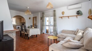 A living room with a sofa, a TV, a dining table, and a kitchen in the background. - Villa 'Liviana' with Mountain View, Pool & Wi-Fi (Cómpeta)