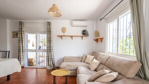 A living room with a beige sofa, a small round table, and a hanging light fixture. - Villa 'Liviana' with Mountain View, Pool & Wi-Fi (Cómpeta)