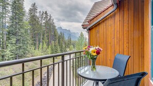 A balcony with a round table and chairs, a vase of flowers, and a view of a forest and mountains. - Call to the Wild in Canmore! (Canmore)