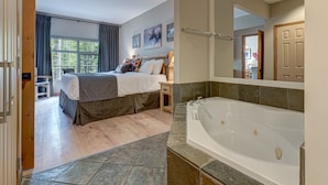 A bedroom with a large bed, a bathroom with a bathtub, and a view of the outdoors. - Call to the Wild in Canmore! (Canmore)