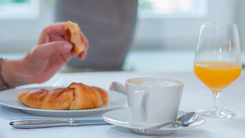 A breakfast setting with a croissant, a cup of coffee, a glass of orange juice, and a spoon on a white table.