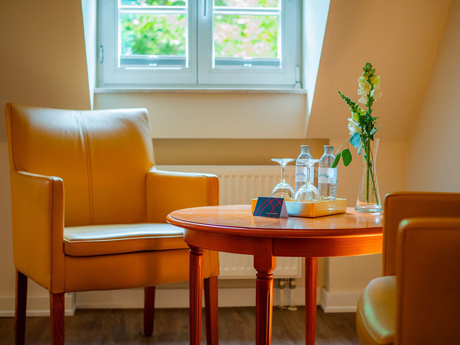 A room with a wooden table, a leather chair, a vase with flowers, and bottles on the table.