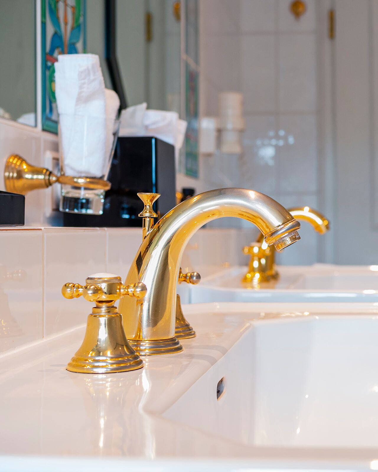 A bathroom with a gold faucet and a mirror reflecting a white towel.