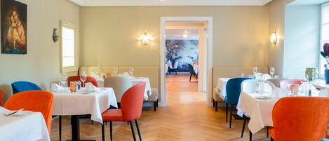 A restaurant with tables set for dining, a chandelier, and a painting on the wall.