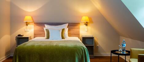 A hotel room with a large bed, two bedside lamps, a small table with a bottle and glass, and a chair.