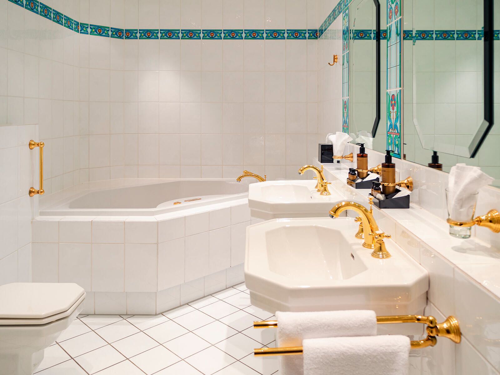 A modern bathroom with a freestanding bathtub, two sinks with gold fixtures, and a toilet.
