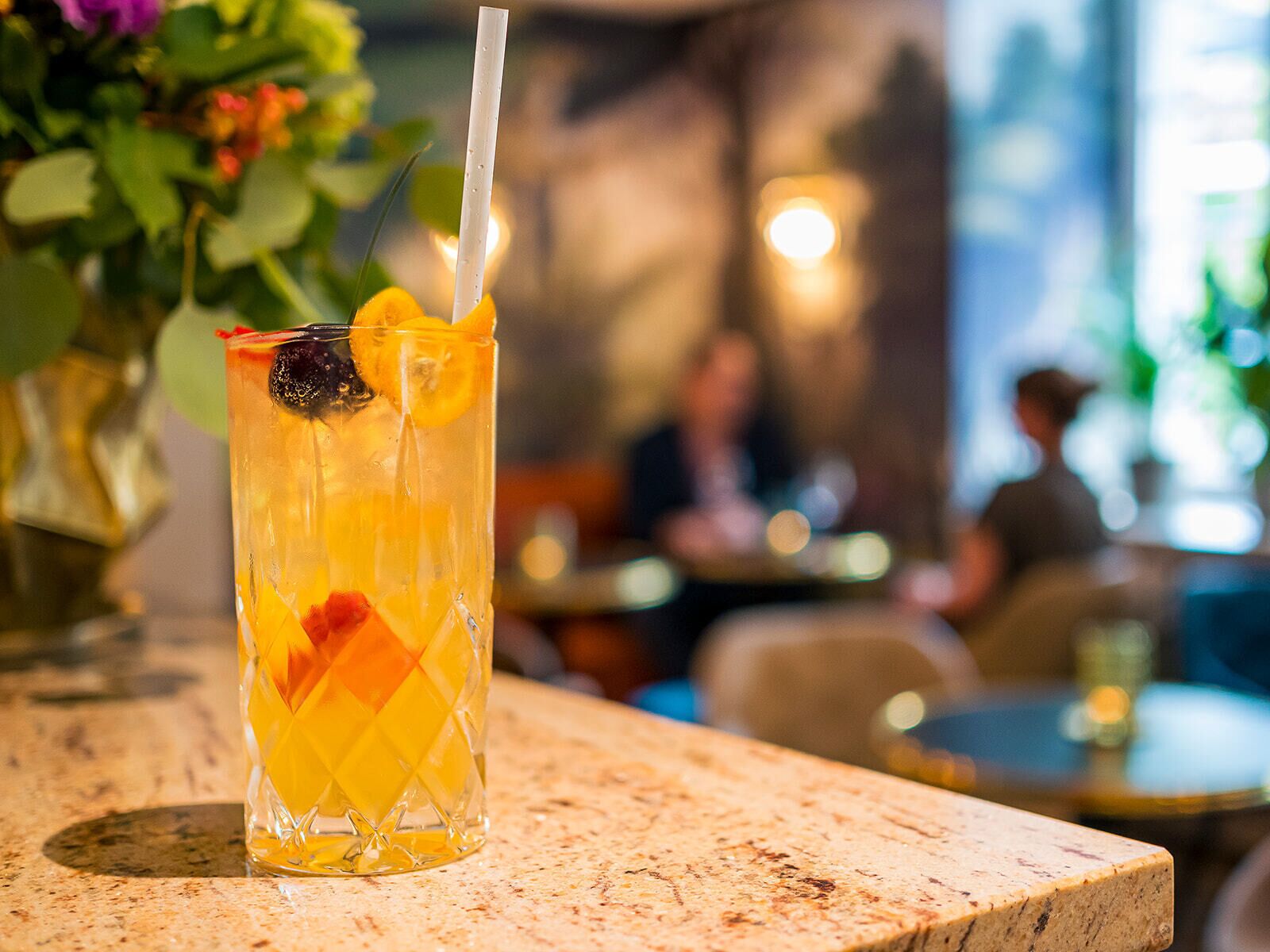 A glass of orange juice with a straw and a slice of lime on a marble table in a restaurant.