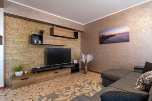 Uma sala de estar com parede de pedra, televisão de tela plana, sofá e um quadro decorativo.