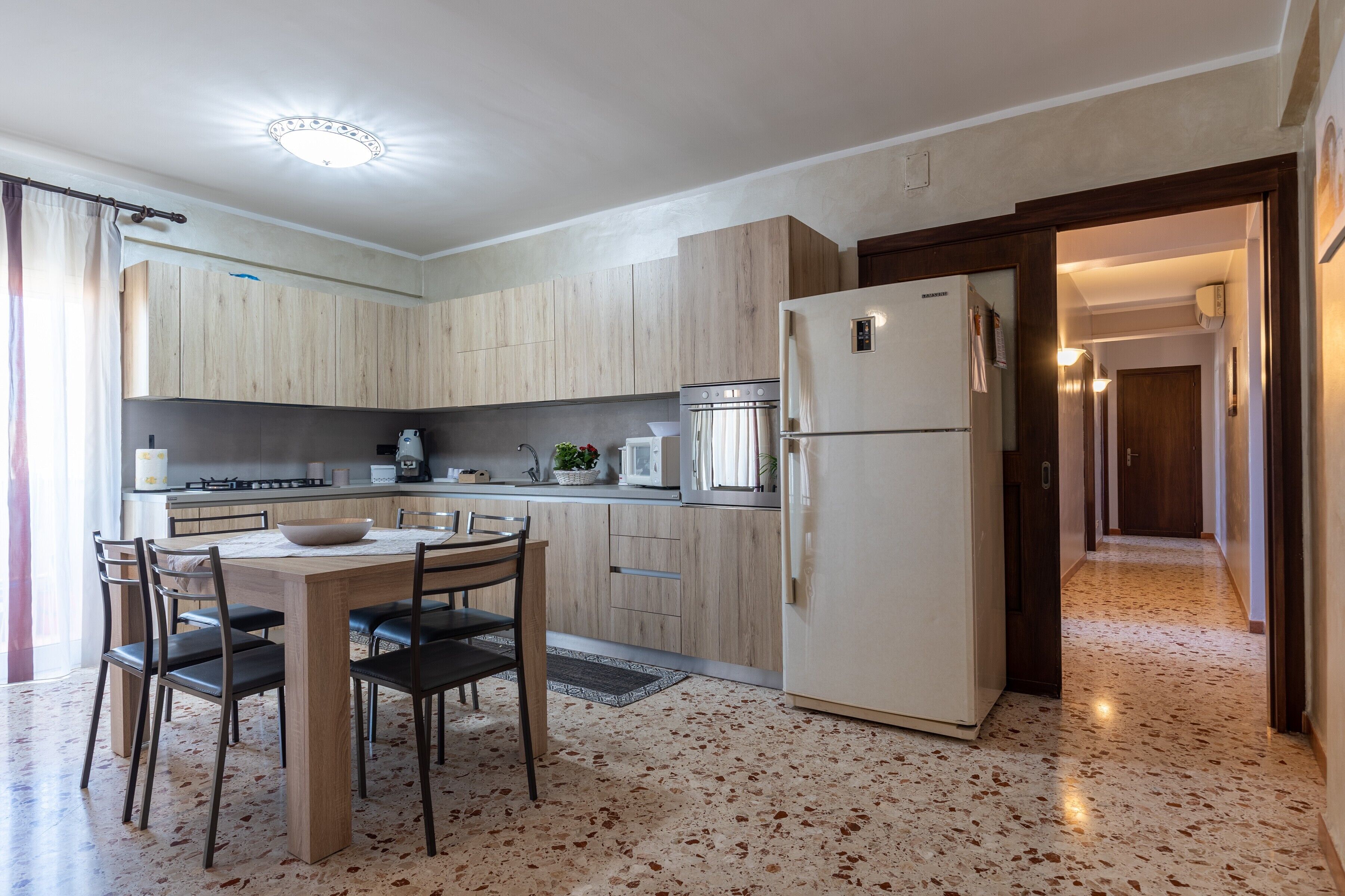 A modern kitchen with wooden cabinets, a dining table with chairs, a refrigerator, and a microwave.