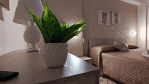 Une chambre à coucher avec un lit, une table de chevet avec une lampe et une plante, un mur décoré d’œuvres d’art et une fenêtre avec des stores.