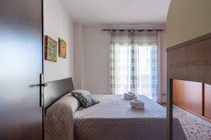 Quarto com cama, almofadas, guarda-roupa e janela com cortinas.