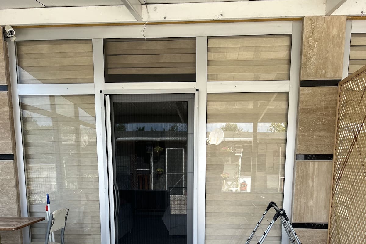 Entrada de un edificio con puerta corredera de vidrio, una silla y una escalera.