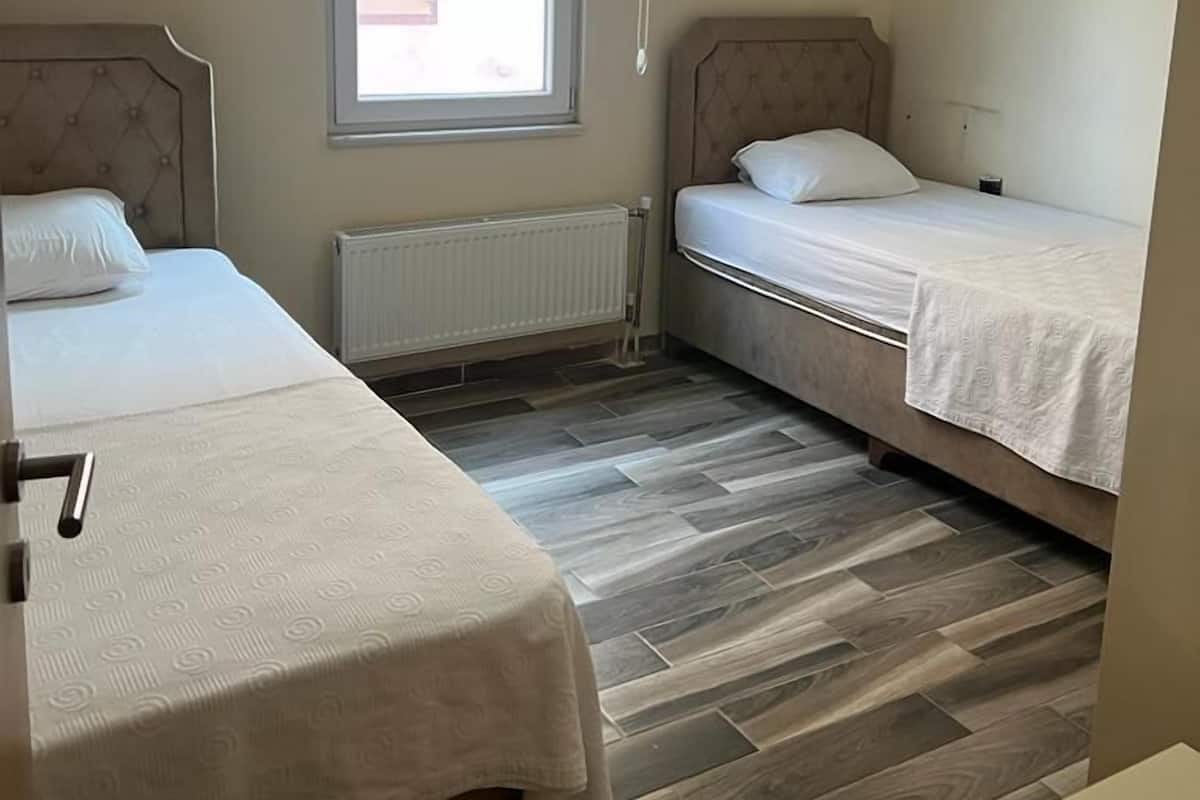 Una habitación pequeña y luminosa con dos camas, una ventana y un radiador.