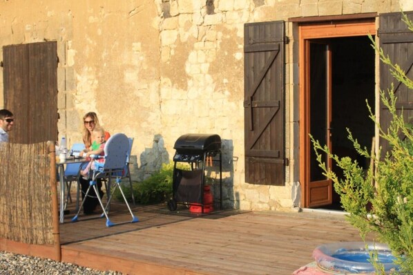 A rustic outdoor dining area with a stone wall, wooden shutters, and a barbecue grill.