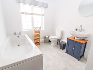 A modern bathroom with a bathtub, toilet, sink, and a wooden shelf with toiletries. - Hill Farm (Nantwich)