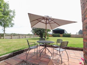 A patio with a table and chairs, a large umbrella, and a brick wall. - Hill Farm (Nantwich)