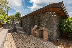 Un edificio in pietra con un'area barbecue in mattoni, una scala che conduce all'interno e un patio lastricato.