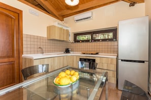 A kitchen with a glass table, a bowl of lemons, wooden cabinets, and a refrigerator. - Holiday Home Casetta delle Rose with A/C and Wi-Fi (Viagrande)