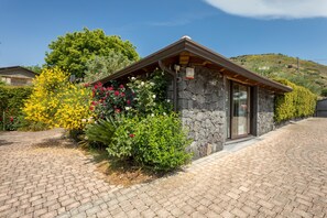 A stone building with a sloped roof, a paved driveway, and a variety of flowering plants. - Holiday Home Casetta delle Rose with A/C and Wi-Fi (Viagrande)