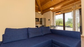 A living room with a blue sectional sofa, wooden ceiling beams, and a view of the outdoors. - Holiday Home Casetta delle Rose with A/C and Wi-Fi (Viagrande)