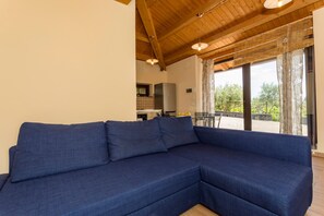Ein Wohnzimmer mit einem blauen Modulsessel, Holzbalkendecke und Blick ins Freie.
