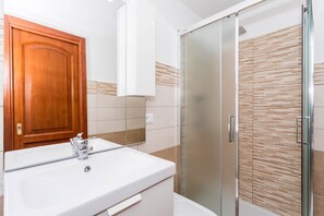 Un bagno con una porta in legno, un lavandino bianco e uno spazio doccia in vetro.