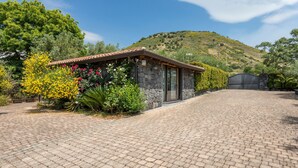A stone building with a tiled roof, surrounded by a paved driveway and lush greenery. - Holiday Home Casetta delle Rose with A/C and Wi-Fi (Viagrande)