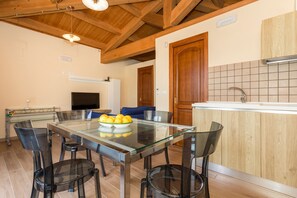 A modern kitchen with a glass dining table, wooden ceiling beams, and a built-in sink. - Holiday Home Casetta delle Rose with A/C and Wi-Fi (Viagrande)