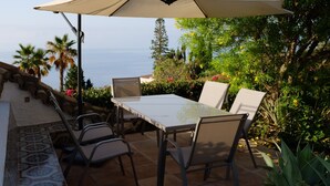 An outdoor patio with a table and chairs, a laptop, and a view of the ocean.