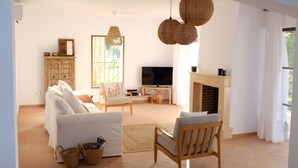 A living room with a sofa, armchair, TV, fireplace, and hanging light fixtures.