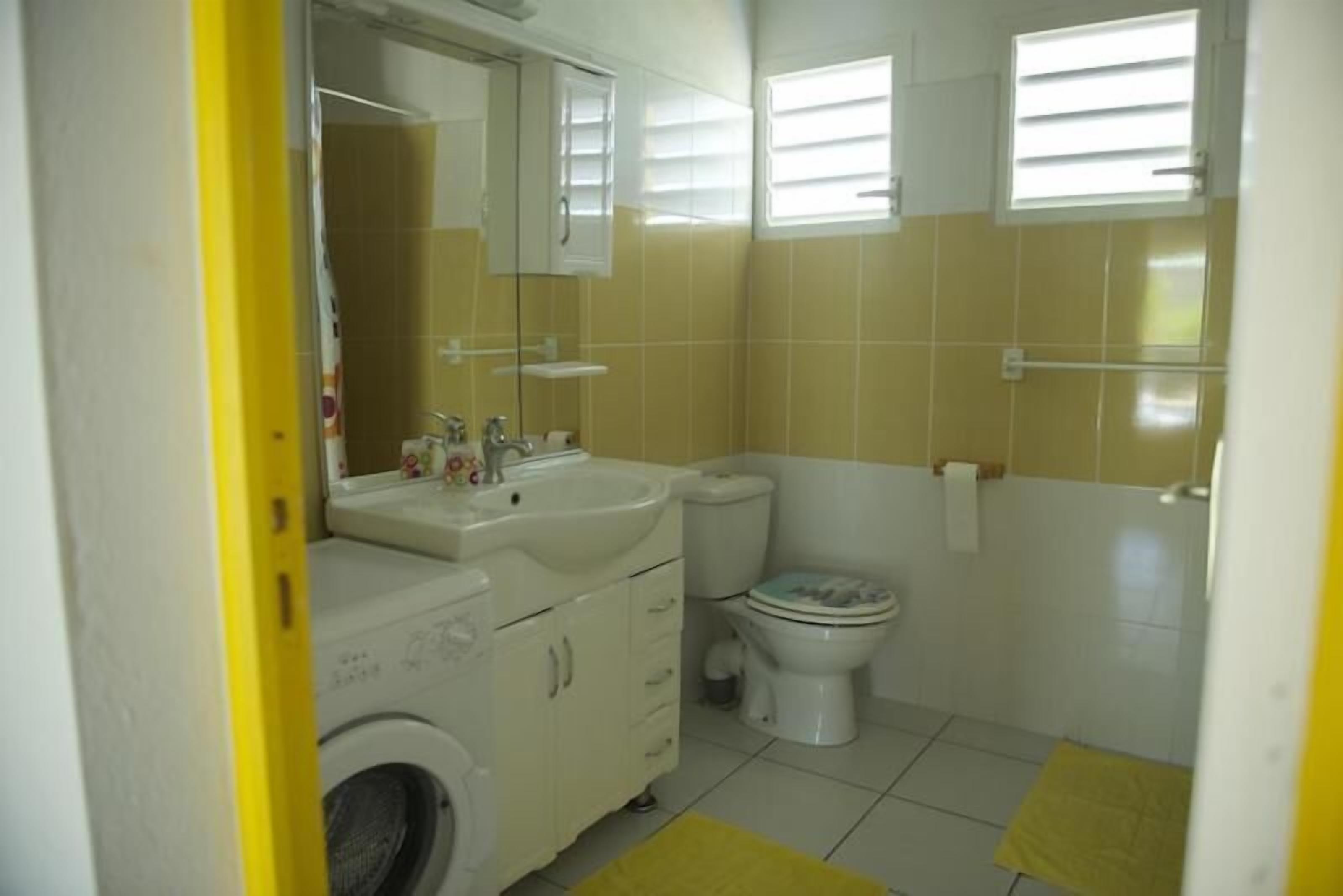 A bathroom with a washing machine, sink, toilet, and a mirror above the sink.
