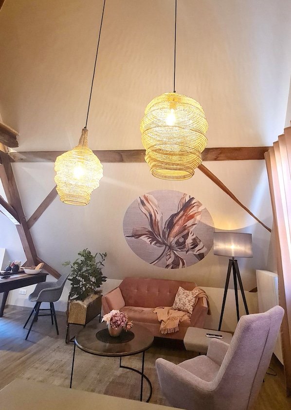 Une pièce confortable avec un canapé, deux fauteuils, une petite table, un lampadaire et deux lampes suspendues.