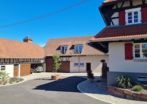 Une rue typique d’un village européen, bordée de bâtiments résidentiels, dont une maison avec un toit en pente et un garage.