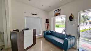 A reception area with a reception desk, a blue sofa, a framed picture on the wall, and a door leading outside. - Asopalav Lawns (Veraval)
