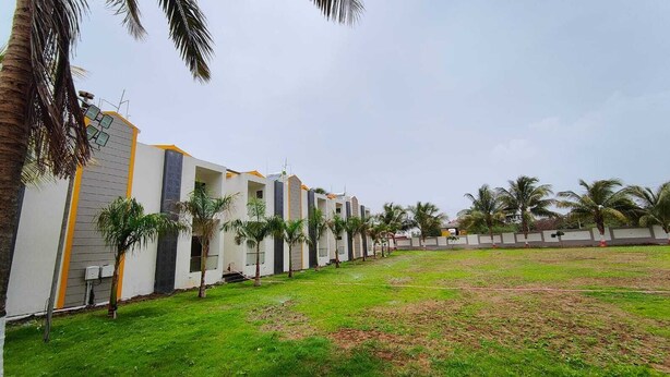 A row of modern buildings with a grassy courtyard and palm trees. - Asopalav Lawns (Veraval)