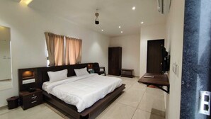 A modern bedroom with a large bed, bedside tables, a wardrobe, and a TV. - Asopalav Lawns (Veraval)