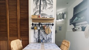 A dining area with a wooden table, wicker chairs, and a wall with a palm tree mural. - Air-conditioned studio with parking and close to the sea. (Carqueiranne)