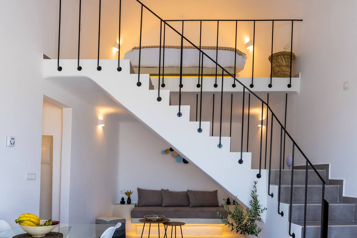 Um interior moderno com escada, sala de jantar com mesa de vidro e área de estar com sofá e planta em vaso.