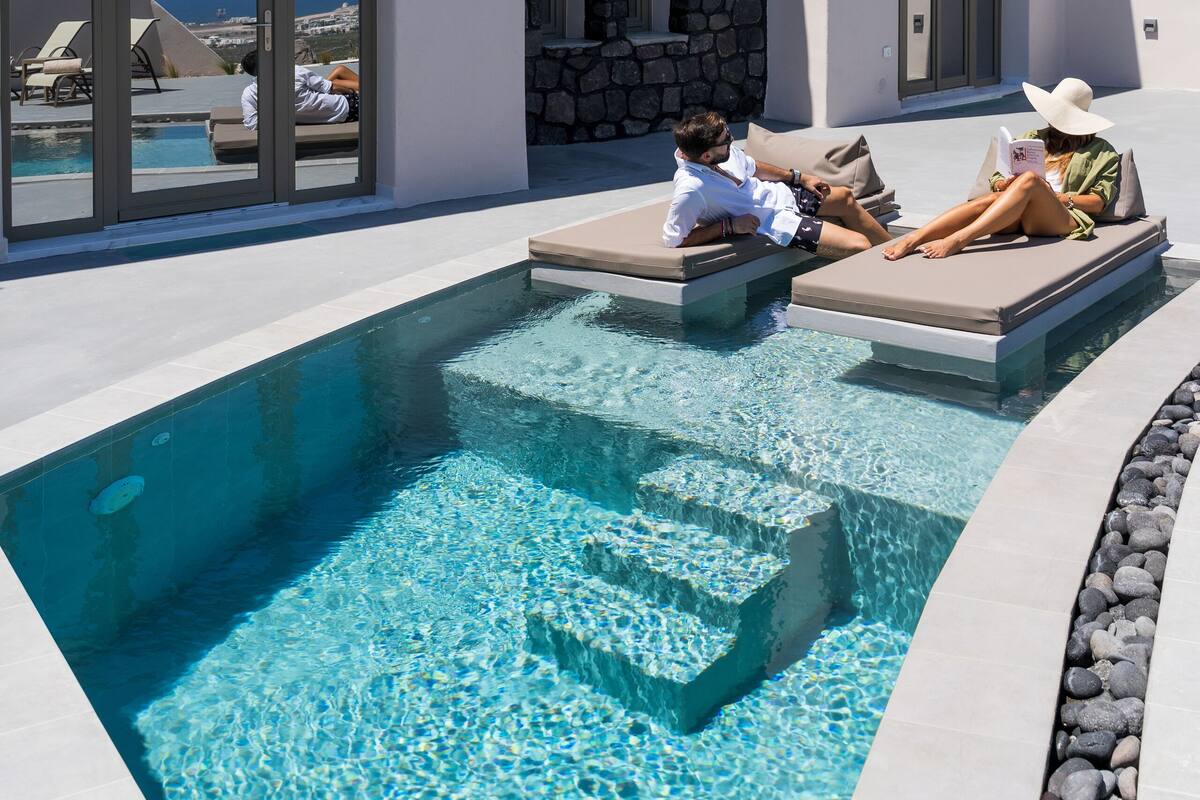 Uma área de piscina moderna com piscina azul cristalina, espreguiçadeiras e um muro de pedra.