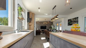 Une cuisine moderne dotée d’un îlot central, d’appareils électroménagers intégrés et d’une grande fenêtre qui laisse entrer la lumière naturelle.
