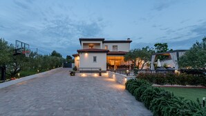Une maison moderne à deux étages, dotée d’une allée pavée menant à une entrée sécurisée par un portail.