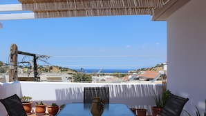 A terrace with a table and chairs, potted plants, and a view of the sea. - Dimokritos Apartment Pitsidia (Pitsidia)
