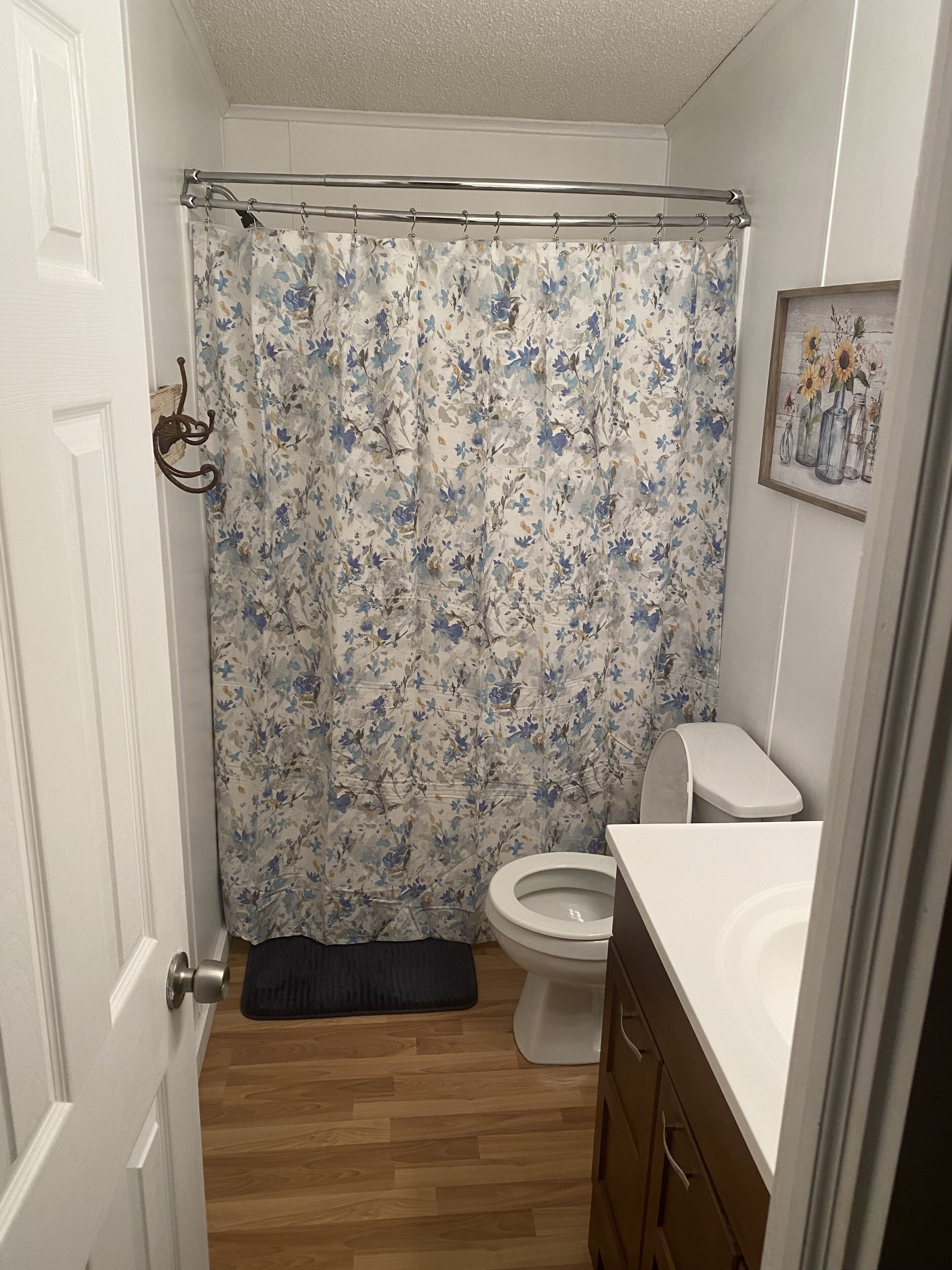 A bathroom with a shower curtain, toilet, and wooden cabinets.